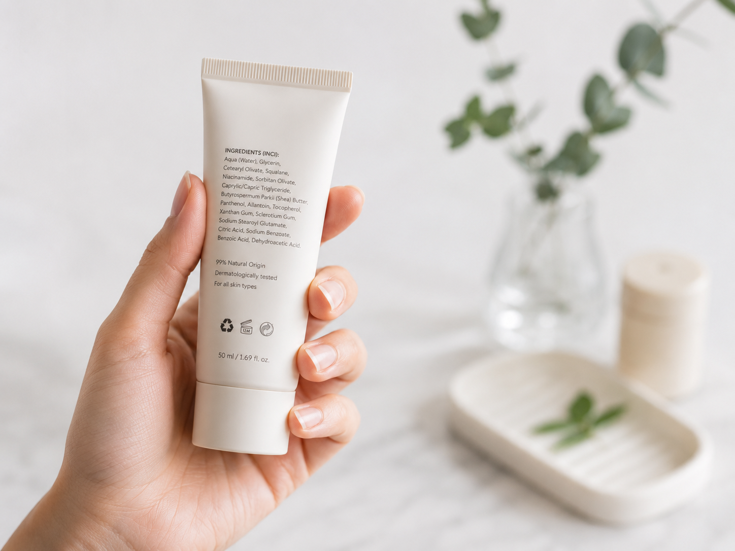 Una mano sosteniendo un envase cosmético minimalista con el listado INCI visible 