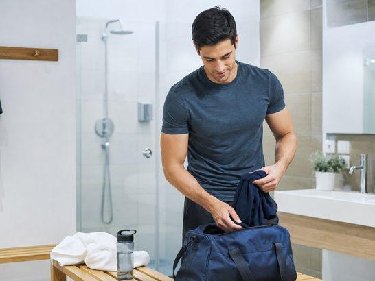Hombre guardando ropa deportiva en una mochila después de hacer ejercicio, con énfasis en higiene, ducha y cambio de ropa