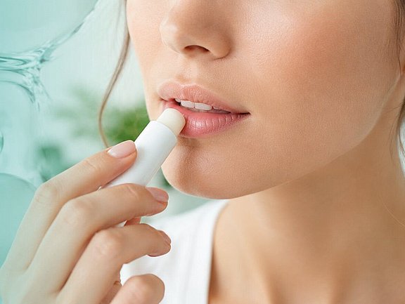 Mujer con herpes labial aplicando con cuidado un bálsamo labial neutro frente a un espejo