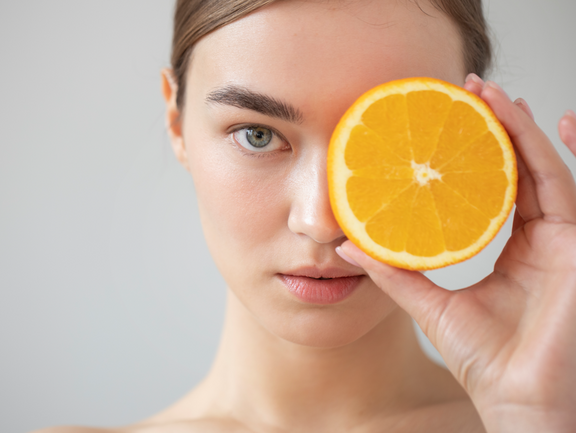 Primer plano de una mujer sujetando una rodaja de naranja simbolizando el uso de la vitamina C en la piel
